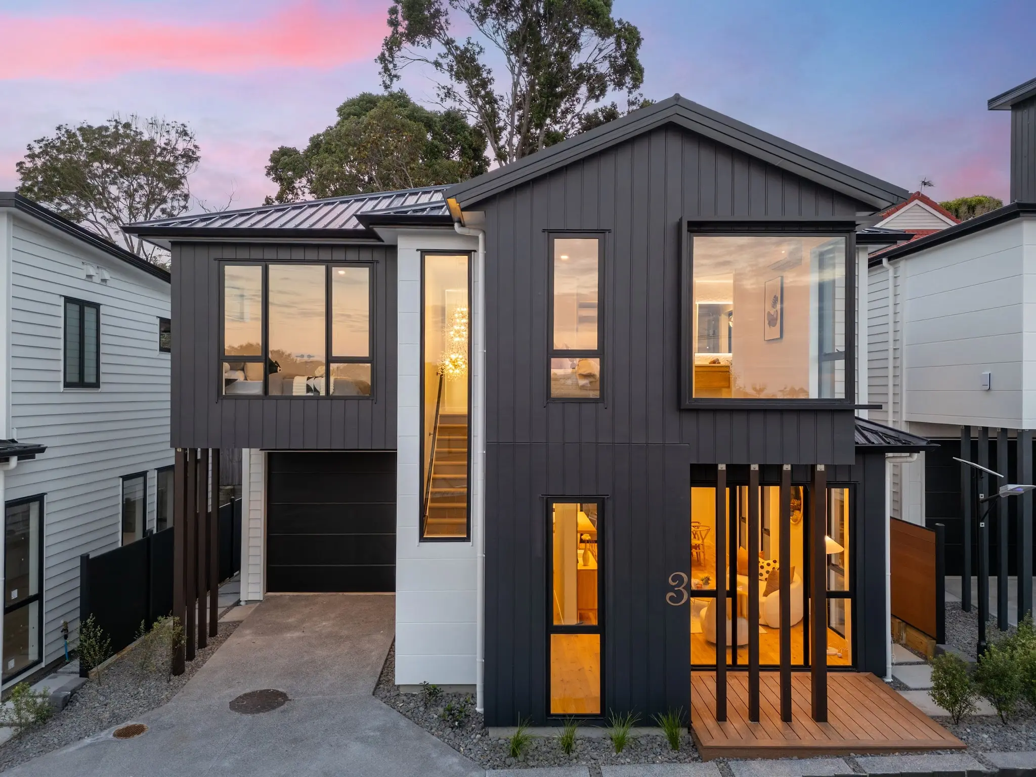 Front elevation at dusk with dark vertical cladding and warm interior light