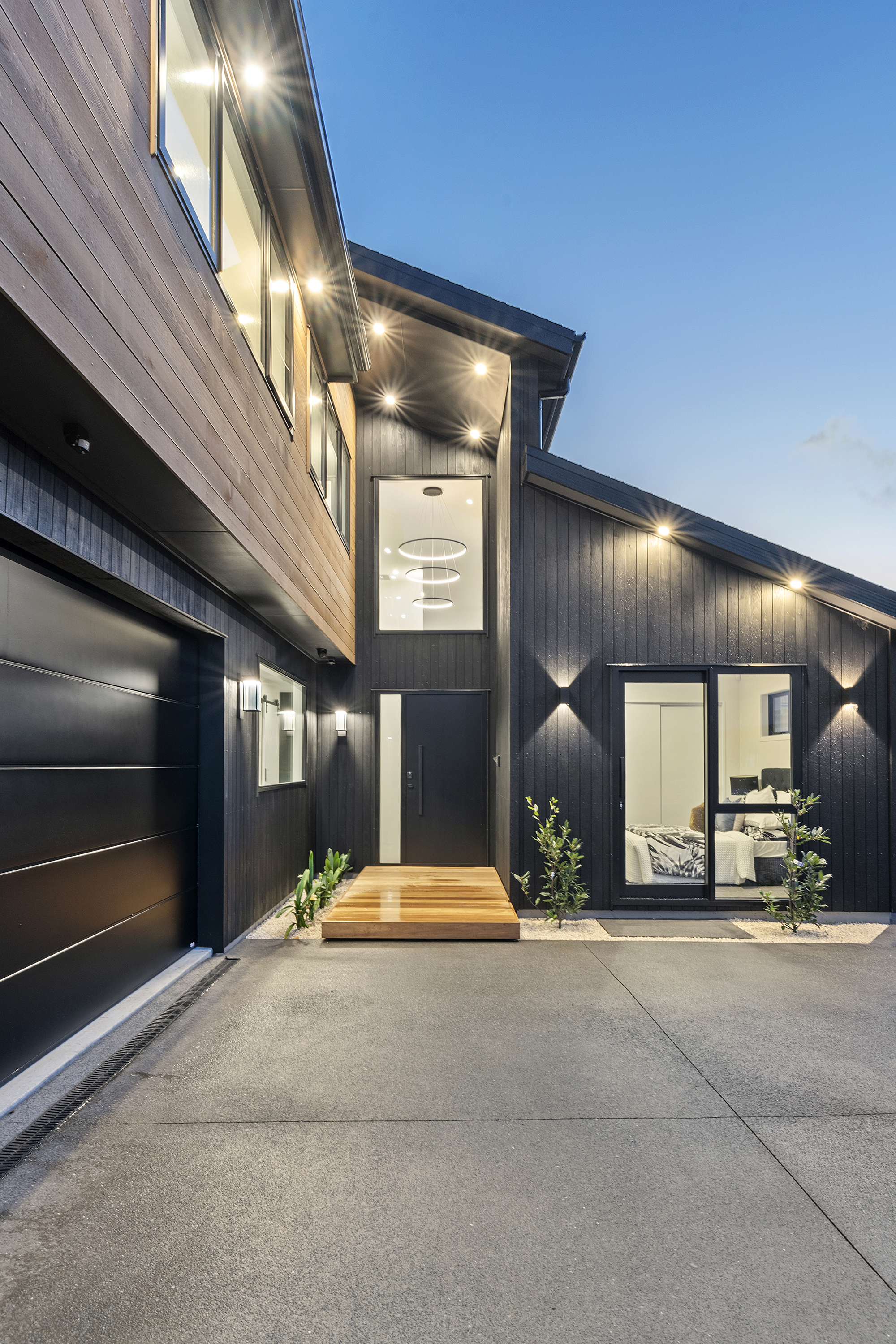 Entry court at 22 Kikorangi Drive with timber steps and dark vertical cladding